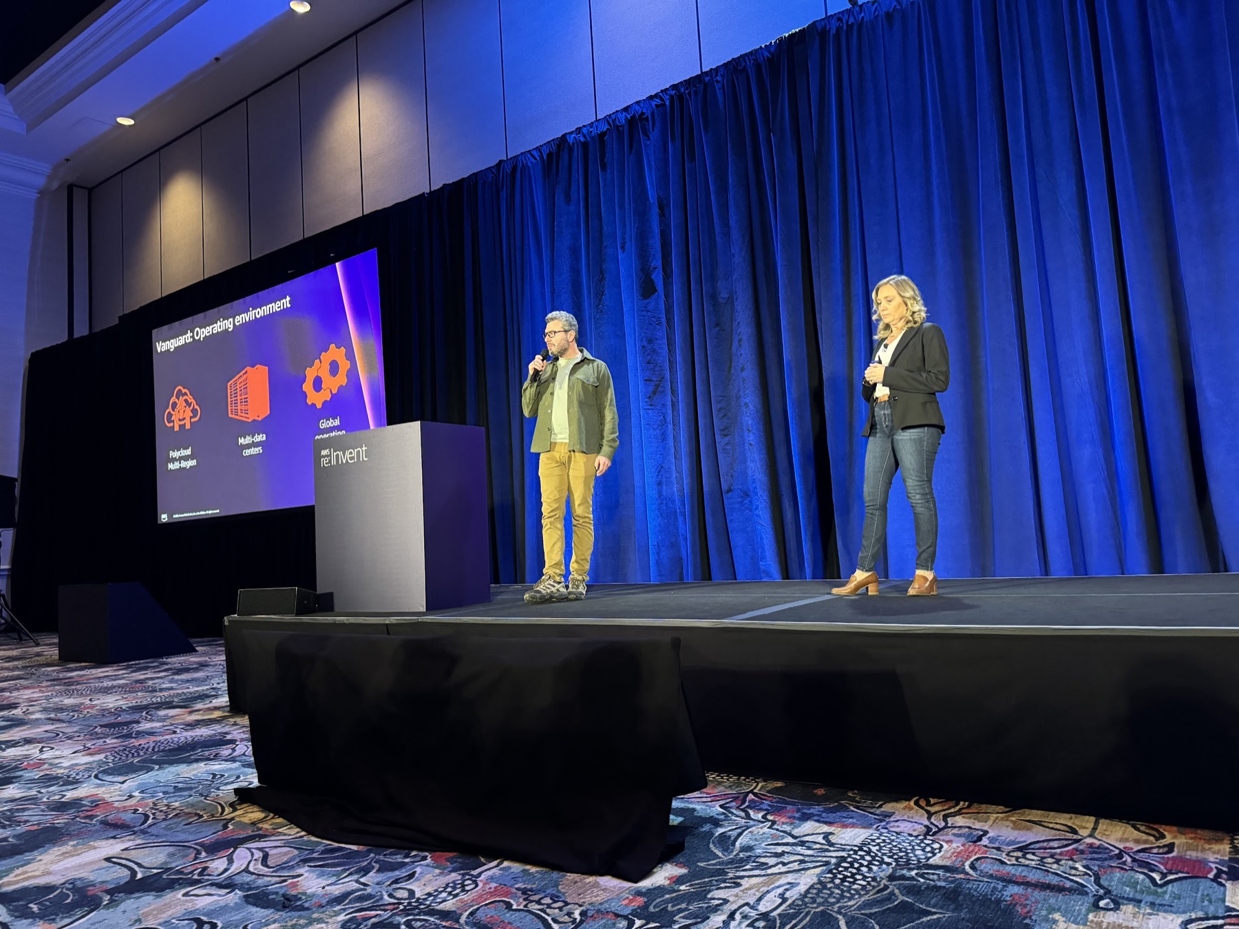 Yoni Ryabinski presenting on the AWS re:Invent main stage in front of a Vanguard operating-environment slide